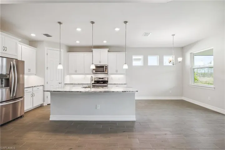 Kitchen with pendant lighting, a kitchen island with sink, appliances with stainless steel finishes, and white cabinets