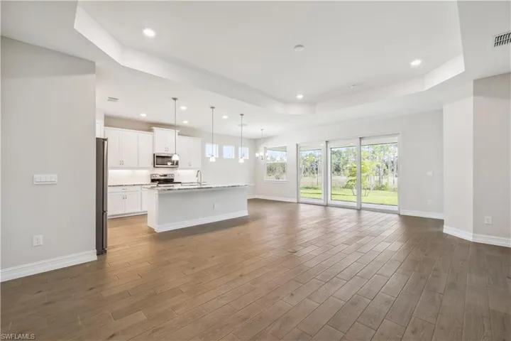 Kitchen featuring white cabinets, hanging light fixtures, a center island with sink, dark wood-type flooring, and appliances with stainless steel finishes