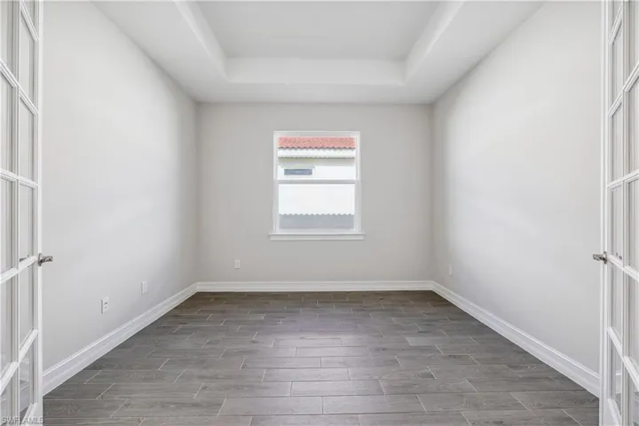 Empty room featuring a tray ceiling, dark wood-type flooring, and french doors