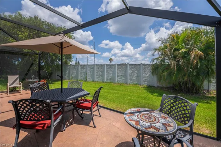 Screened-in patio featuring stamped concrete flooring, a manicured lawn, a privacy fence, and mature landscaping