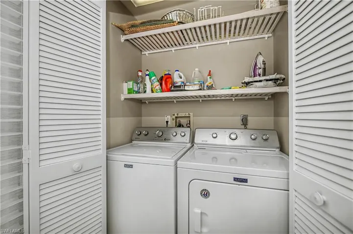 Dedicated laundry closet featuring louvered bi-fold doors, two white appliances, and two upper wire shelving units
