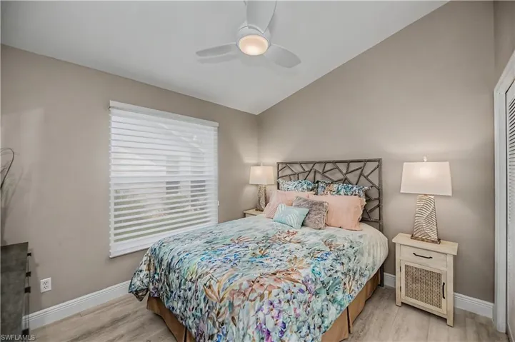 Bedroom featuring vaulted ceilings, wood-finish flooring, a window with horizontal blinds, a ceiling fan with integrated lighting, and a louvered closet door