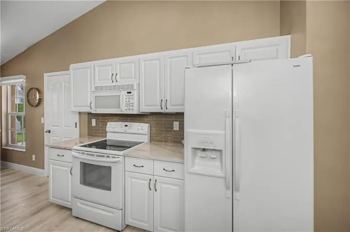 Kitchen featuring white cabinetry, stone-finish countertops, and a full suite of white appliances including a side-by-side refrigerator, electric range, and microwave