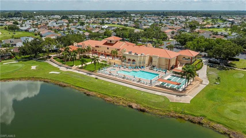 Clubhouse building with a terracotta-style roof, featuring multiple swimming pools, surrounding green spaces, and a body of water