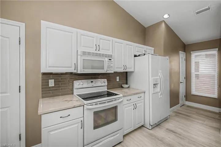 Kitchen featuring white cabinetry, light-toned countertops, a tile backsplash, and light wood-finish flooring