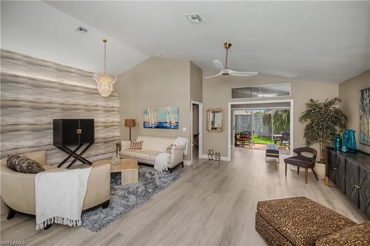 Vaulted ceilings featuring a chandelier and ceiling fan, wood-finish flooring, and a textured accent wall