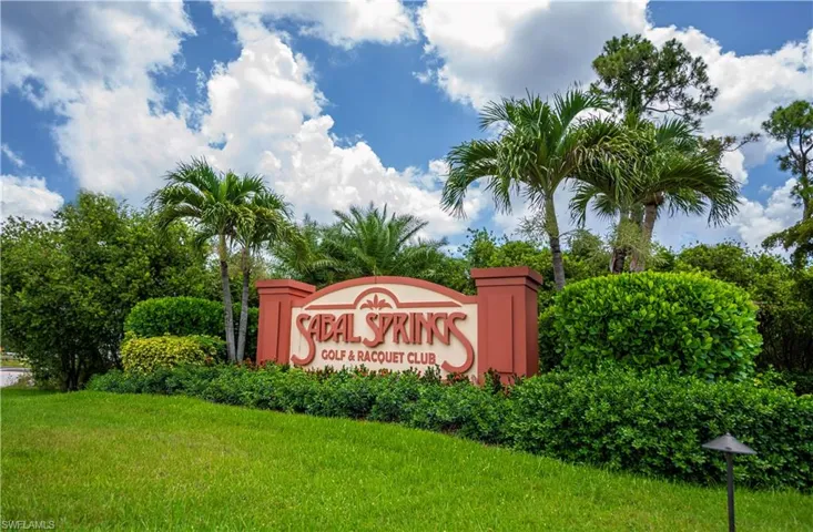 Entryway sign for Sabal Springs Golf & Racquet Club, framed by lush tropical landscaping