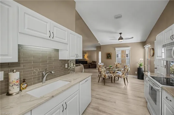 Kitchen and dining area featuring white cabinetry, light-toned countertops, a rectangular undermount sink with a gooseneck faucet, a gray glass subway tile backsplash, and light wood-finish flooring