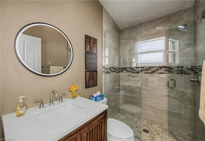 Contemporary bathroom featuring a glass-enclosed shower with stone-finish tile walls and a mosaic accent band