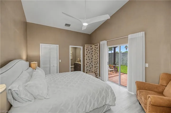 Vaulted ceiling with a ceiling fan, white wood-finish flooring, sliding glass patio doors, and a private enclosed patio with terracotta-style pavers