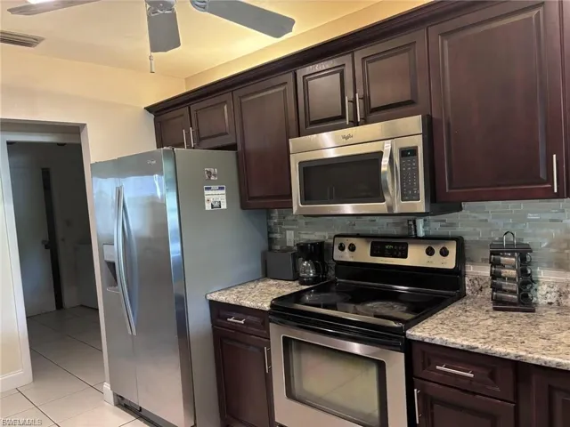 Kitchen with appliances with stainless steel finishes, dark brown cabinetry, decorative backsplash, light tile patterned flooring, and a ceiling fan