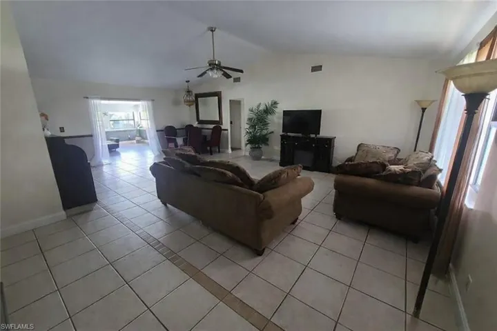 Living room featuring light tile patterned floors, a ceiling fan, and vaulted ceiling