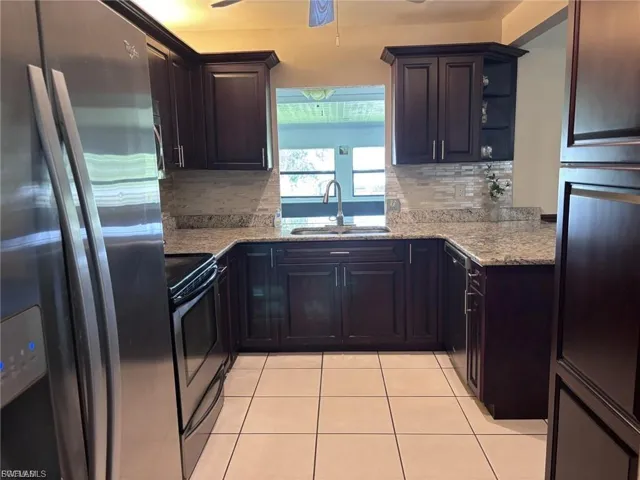 Kitchen featuring stainless steel refrigerator with ice dispenser, black electric range, light tile patterned floors, and light stone counters