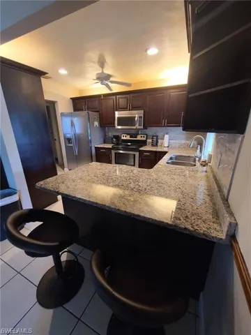 Kitchen featuring a breakfast bar area, dark brown cabinets, light tile patterned floors, a peninsula, and stainless steel appliances