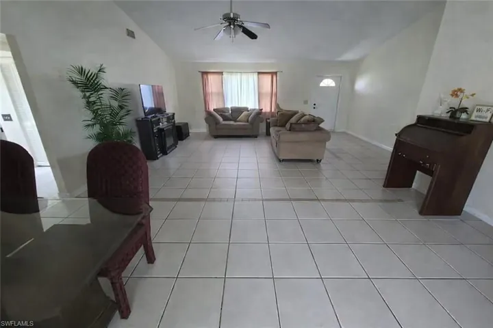 Living area with vaulted ceiling, light tile patterned floors, and a ceiling fan