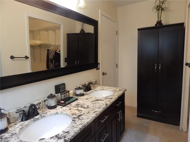 Bathroom with double vanity, light tile patterned floors, and a walk in closet