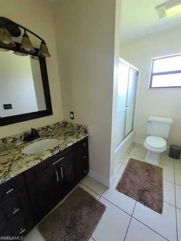 Full bathroom featuring vanity, light tile patterned floors, and combined bath / shower with glass door