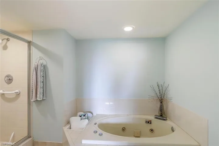Built-in jetted tub with tiled surround, adjacent to a glass-enclosed shower separate.