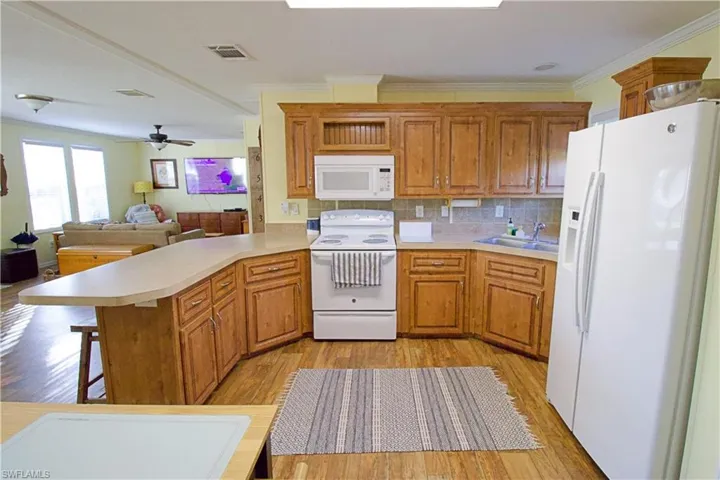Kitchen with kitchen peninsula, a breakfast bar, white appliances, ceiling fan, and sink