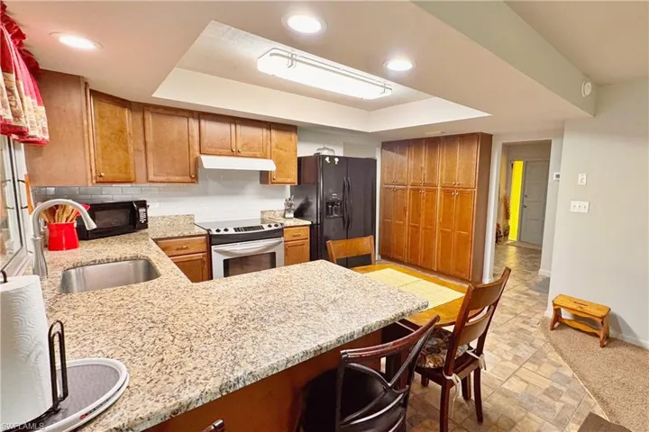 Kitchen featuring kitchen peninsula, a tray ceiling, light stone countertops, and black appliances