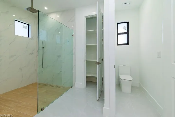 Full bathroom with a marble finish shower, a spacious closet, plenty of natural light, and toilet