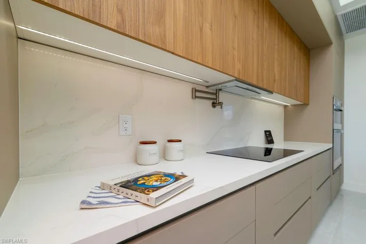 Kitchen featuring black electric stovetop, modern cabinets, light stone counters, stainless steel double oven, and range hood