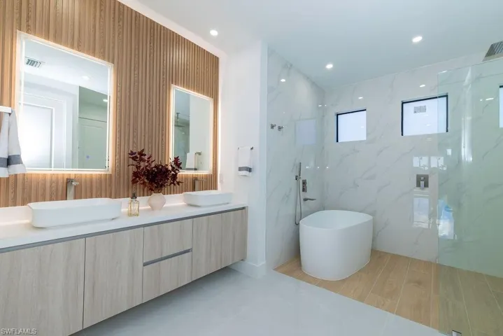 Full bath with double vanity, a freestanding bath, a marble finish shower, and recessed lighting