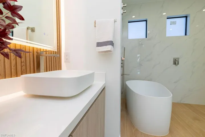 Bathroom with vanity, a freestanding tub, tile walls, and a marble finish shower