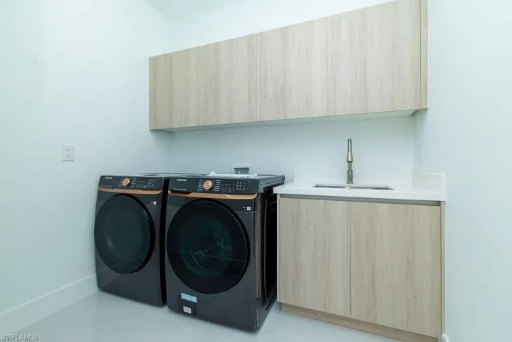 Washroom with cabinet space, washer and clothes dryer, baseboards, and light tile patterned floors