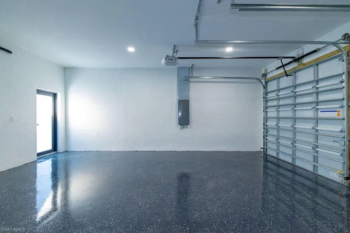 Garage with a garage door opener, electric panel, and recessed lighting