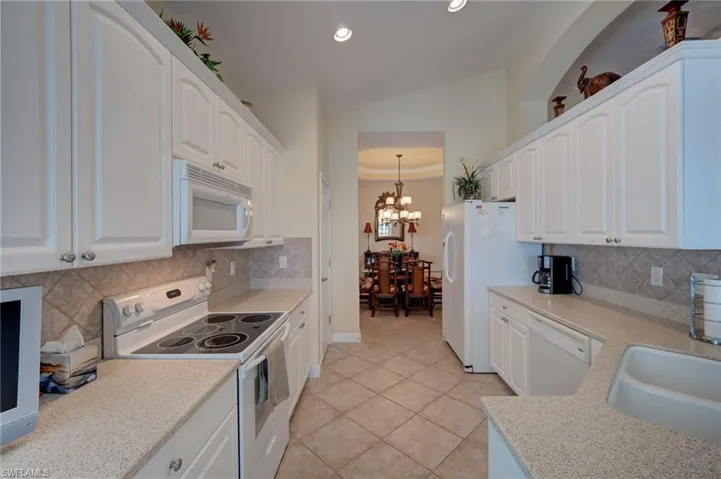 Kitchen with white appliances, white cabinets, a raised ceiling, backsplash, and light tile patterned floors