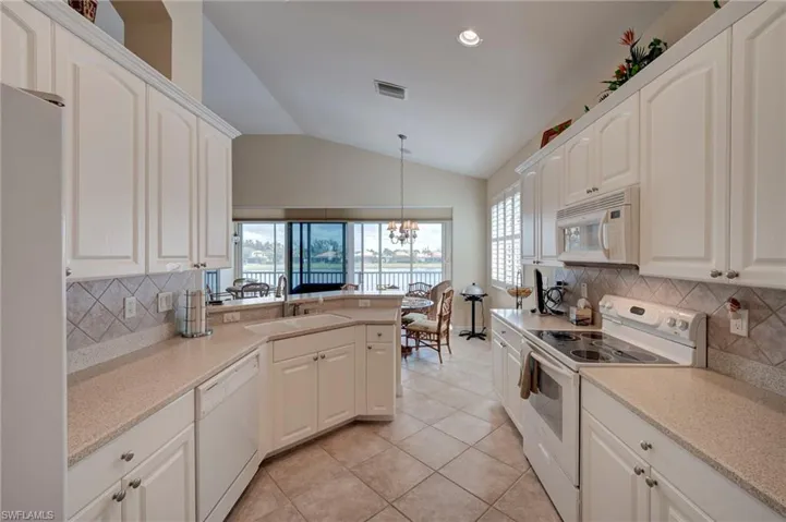 Kitchen with white appliances, tasteful backsplash, lofted ceiling, a peninsula, and white cabinetry