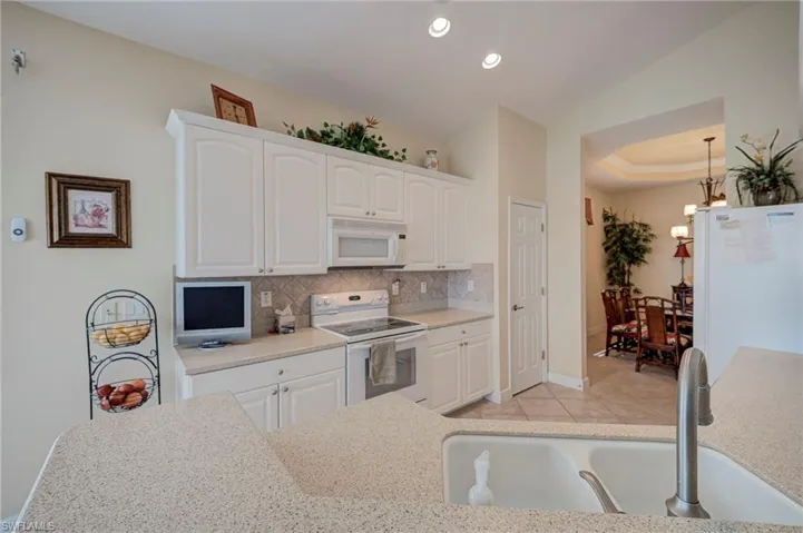 Kitchen with white appliances, white cabinetry, backsplash, light tile patterned flooring, and a raised ceiling