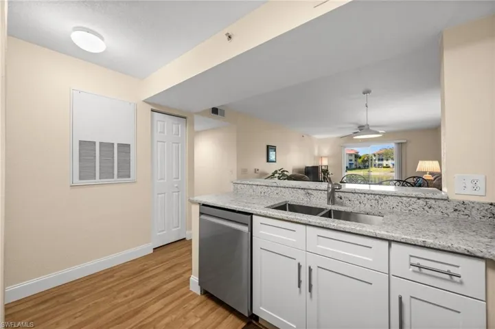 Kitchen with a peninsula, dishwasher, light stone countertops, white cabinetry, and ceiling fan