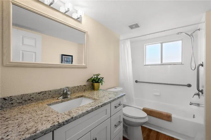 Full bathroom with vanity, shower / tub combo with curtain, dark wood-style flooring, and a textured wall