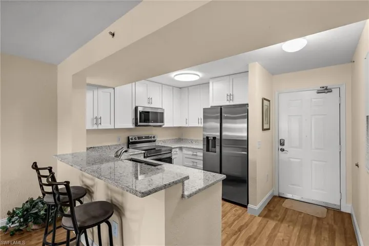 Kitchen featuring light stone counters, a peninsula, stainless steel appliances, a kitchen breakfast bar, and white cabinets