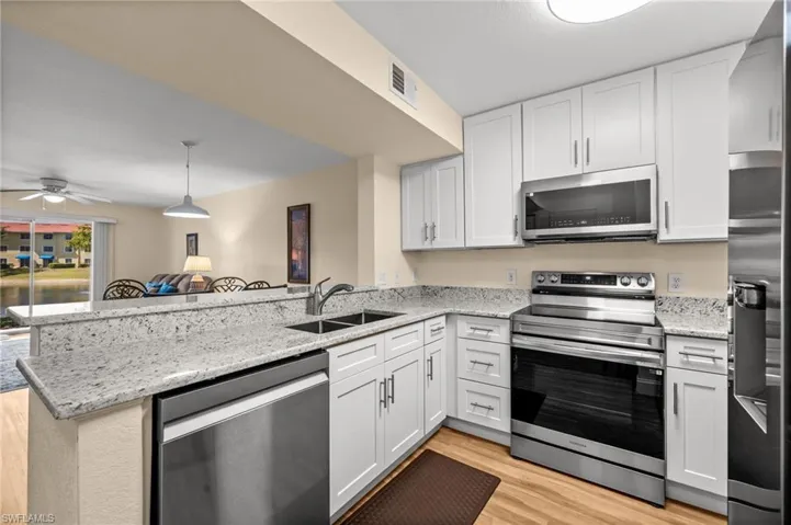 Kitchen featuring stainless steel appliances, light stone countertops, a peninsula, a ceiling fan, and light wood-style flooring