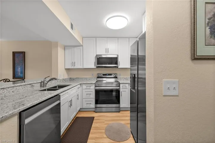 Kitchen featuring a textured wall, stainless steel appliances, light stone counters, white cabinetry, and light wood finished floors