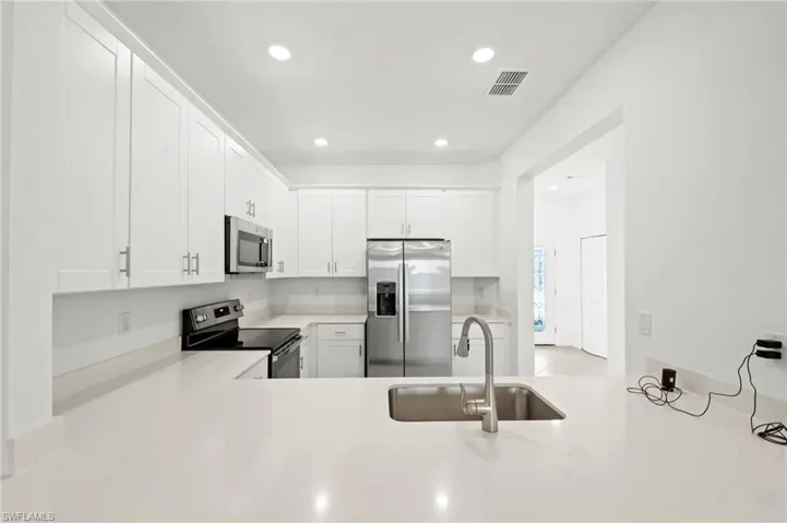 Kitchen with stainless steel appliances, white cabinetry, recessed lighting, light stone countertops, and a peninsula