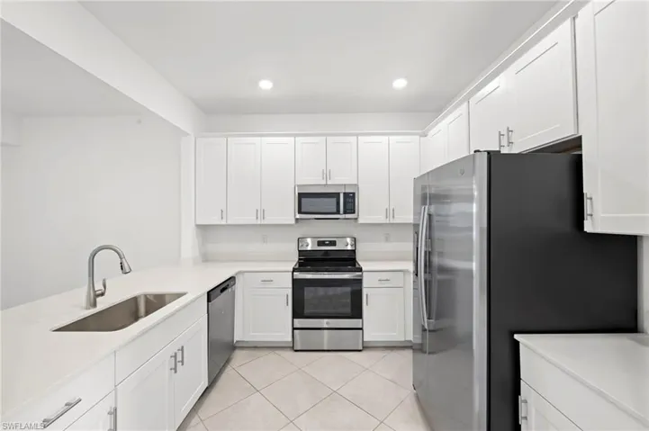 Kitchen with stainless steel appliances, white cabinets, light tile patterned floors, recessed lighting, and light stone countertops