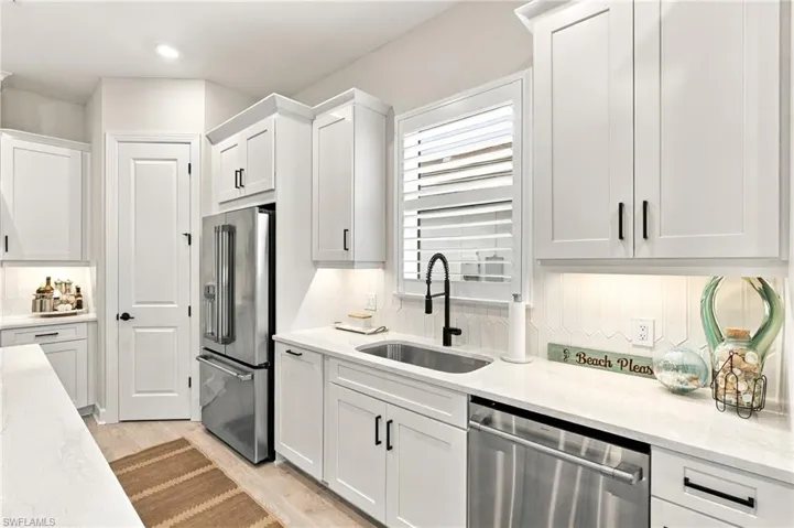 Elegant casual dining area featuring designer pendant lighting, built-in GE Café appliances, glass-front cabinetry, and expansive sliding glass doors opening to the outdoor kitchen and covered lanai. Indoor-outdoor living at its finest!