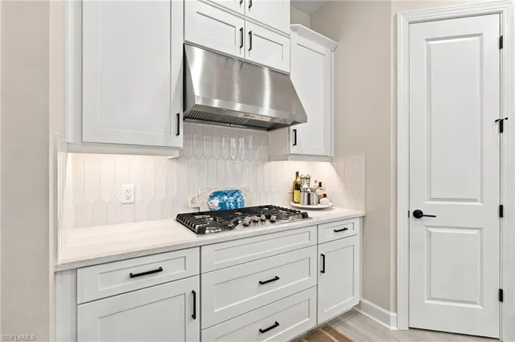 Chef-inspired kitchen featuring a five-burner gas cooktop, sleek stainless steel hood, elegant white shaker cabinetry, quartz countertops, and contrasting matte-black hardware.