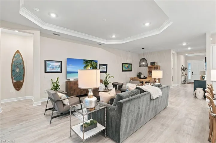 Spacious, light-filled great room featuring an elegant tray ceiling, recessed lighting, designer finishes, and beautiful wood-look flooring. The impressive 85-inch television conveys with the home!