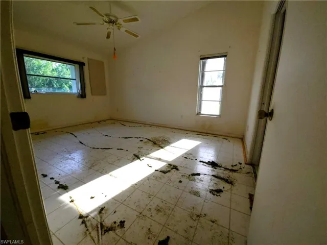 Empty room featuring healthy amount of natural light, tile patterned floors, lofted ceiling, and a ceiling fan