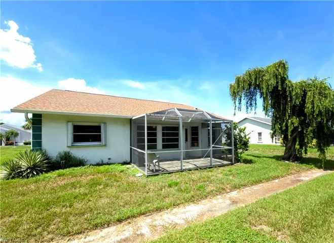 Rear view of property with a lawn, stucco siding, a patio, a lanai, and roof with shingles