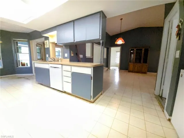Kitchen with white dishwasher, lofted ceiling, light countertops, gray cabinetry, and hanging light fixtures