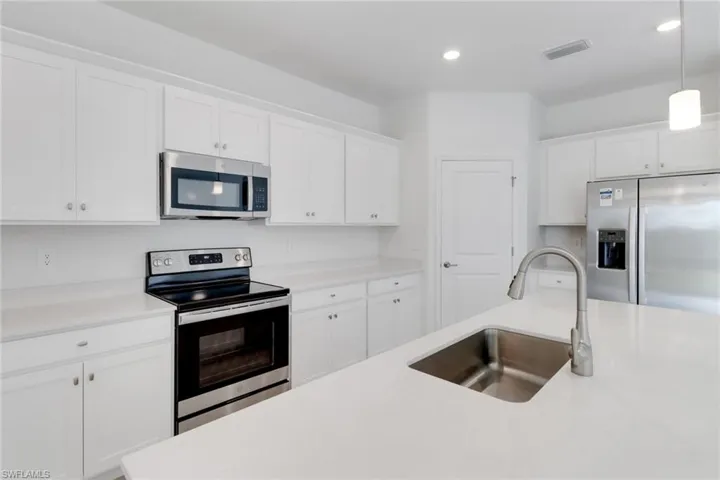 Kitchen with stainless steel appliances, a sink, white cabinetry, light countertops, and decorative light fixtures