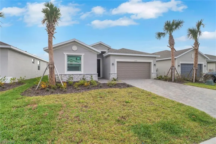 Ranch-style home featuring decorative driveway, stucco siding, a garage, stone siding, and a front lawn