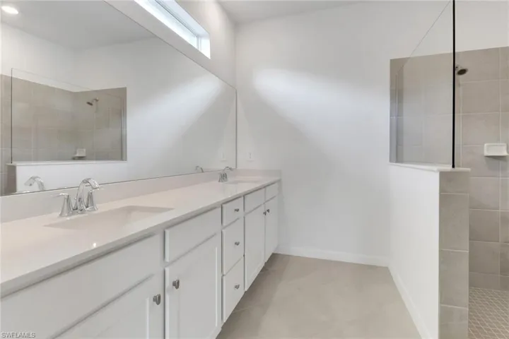 Bathroom with a walk in shower, double vanity, a sink, and baseboards