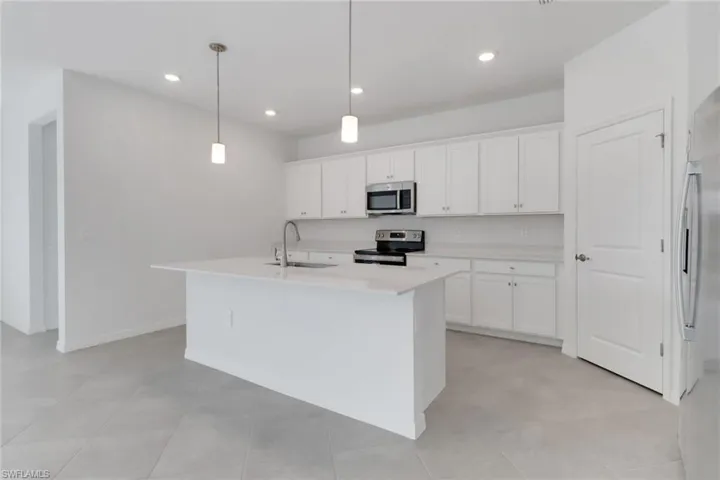 Kitchen featuring decorative light fixtures, a center island with sink, light countertops, appliances with stainless steel finishes, and a sink